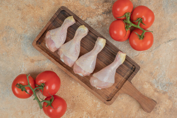 fresh tomatoes with wooden board of uncooked chicken legs